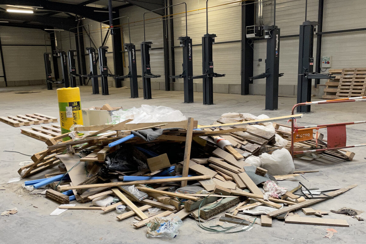 Amas de chutes de chantier — bois, palettes, emballages — au sol d’un atelier neuf, avant évacuation et nettoyage de livraison.
