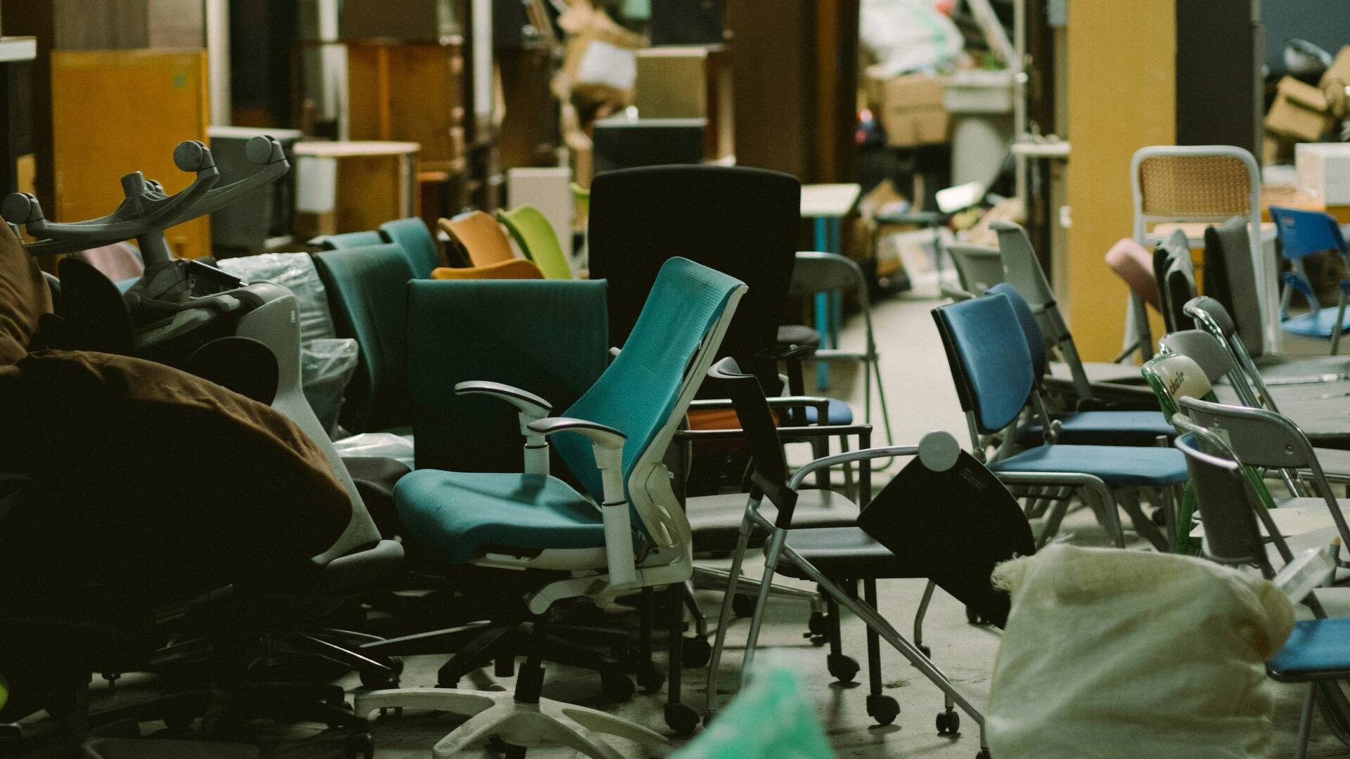 Salle encombrée de chaises et de mobilier empilés, sans passage dégagé au sol.