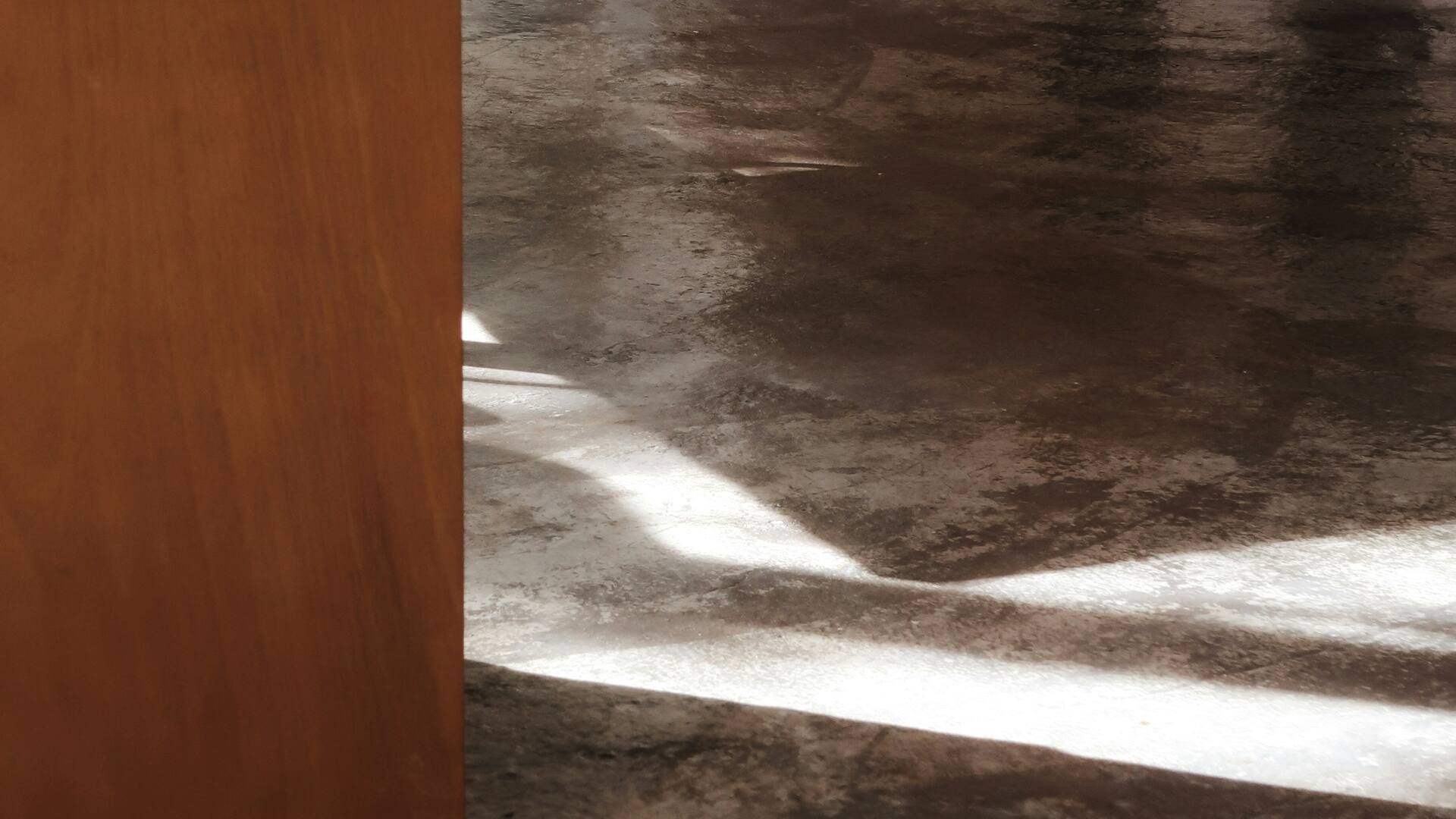 Sol en béton ciré traversé par une bande de lumière, avec les traces d’usure du passage.