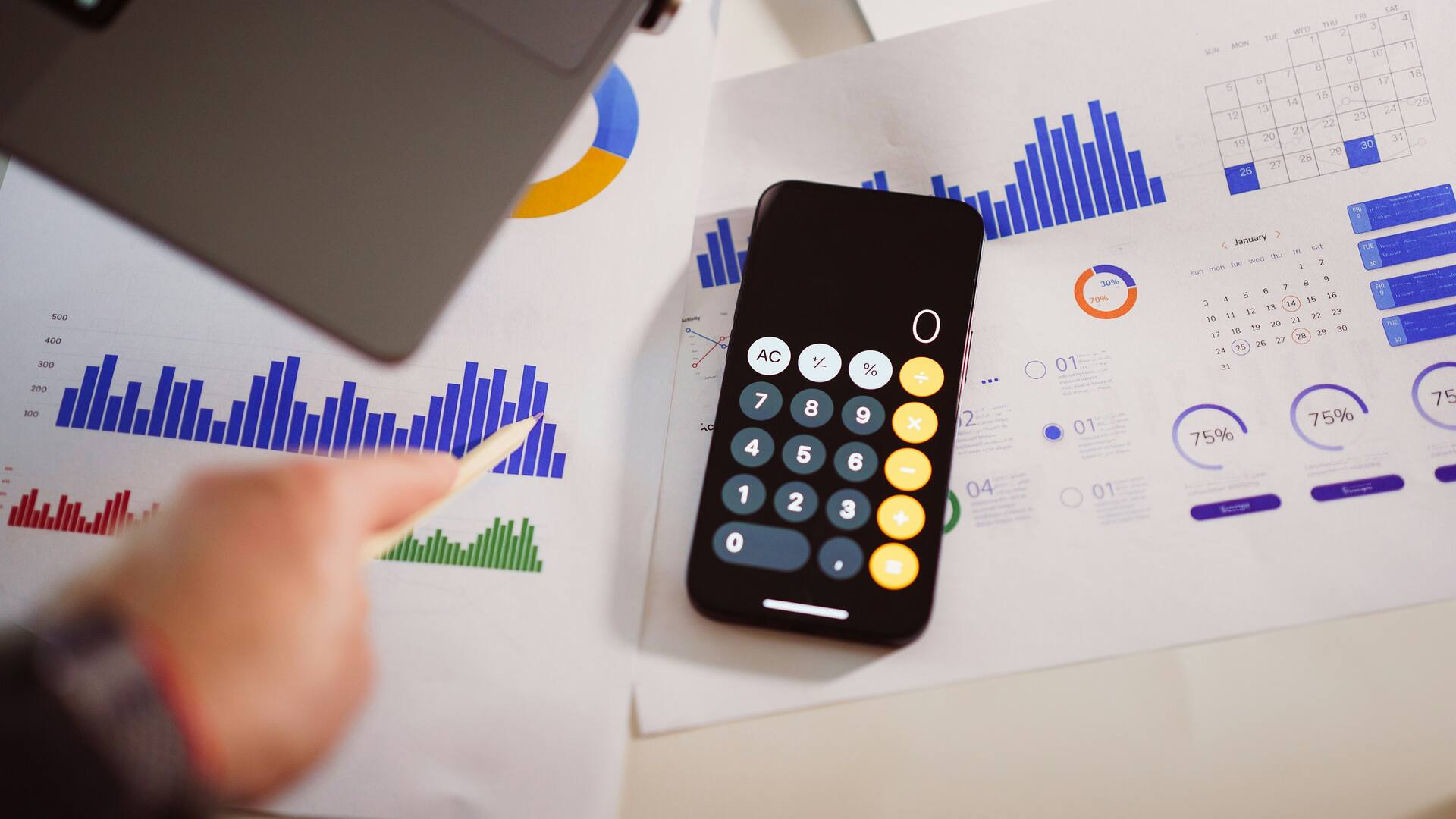 Une calculatrice et des graphiques imprimés étalés sur un bureau, avec un crayon posé dessus.