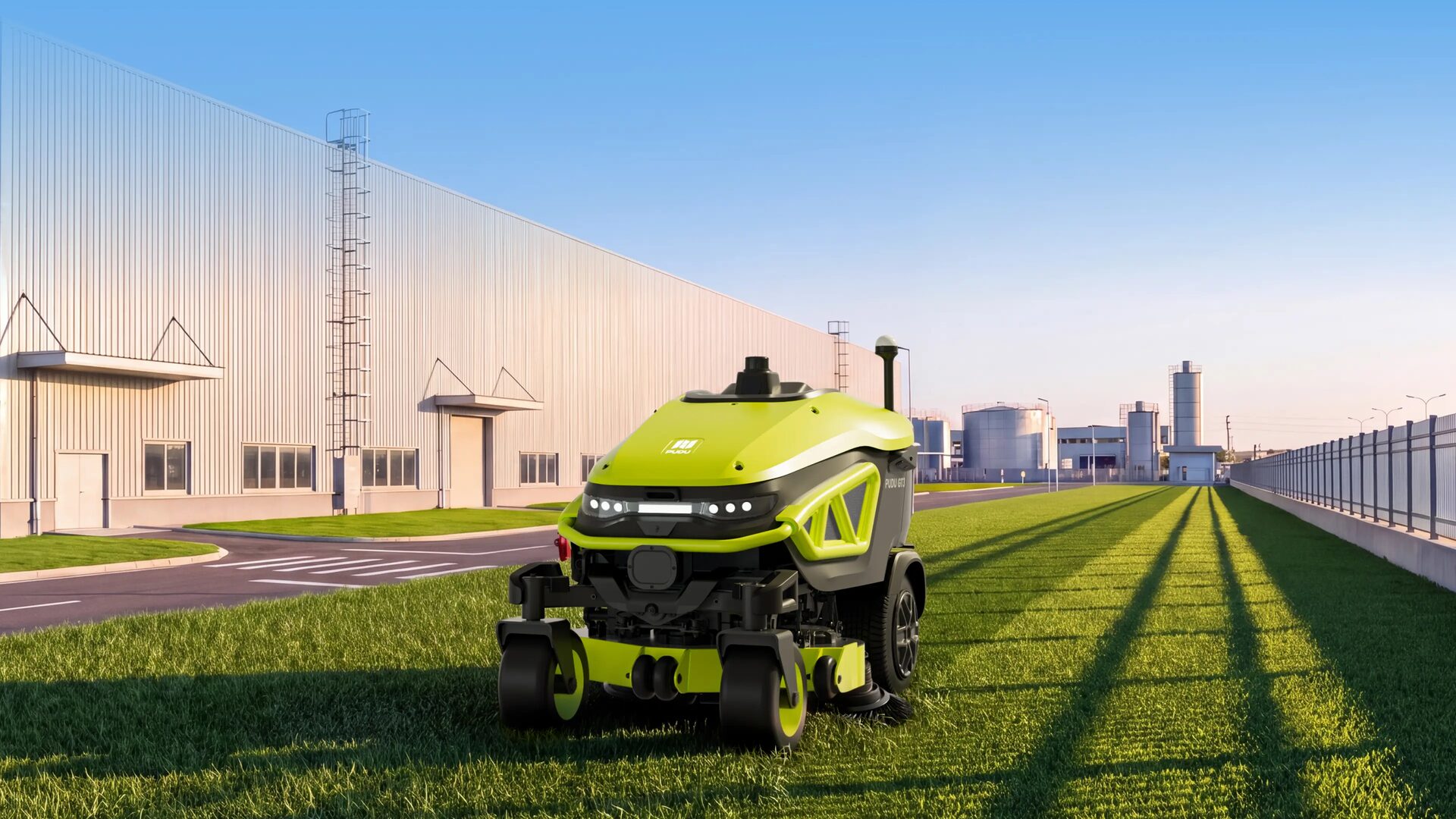 Robot de tonte PUDU GT3, vert et noir, sur une bande de pelouse le long d’un bâtiment industriel.