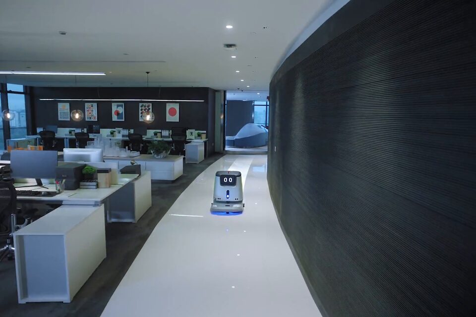 Autolaveuse autonome de la série PUDU CC1 en service dans l’allée centrale d’un plateau de bureaux, entre des postes de travail inoccupés.
