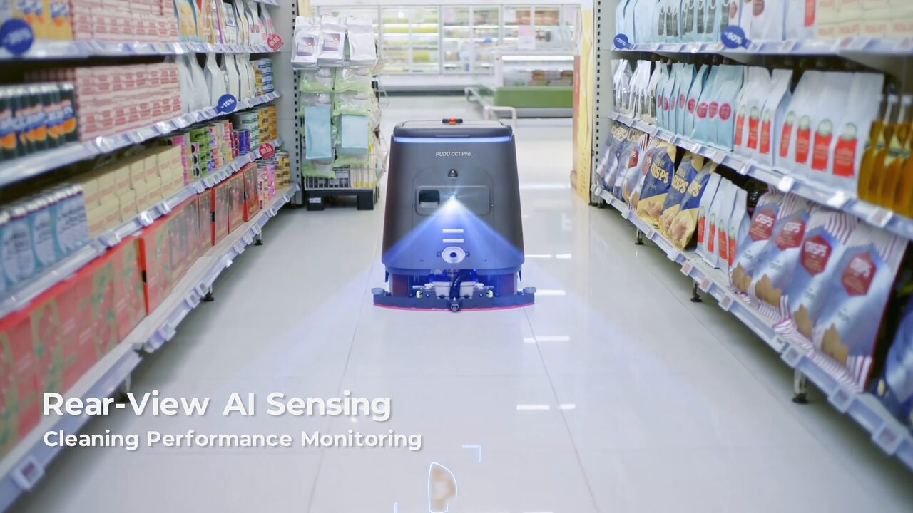 Autolaveuse autonome PUDU CC1 Pro vue de dos dans une allée de magasin, le faisceau de sa caméra arrière projeté au sol derrière elle.