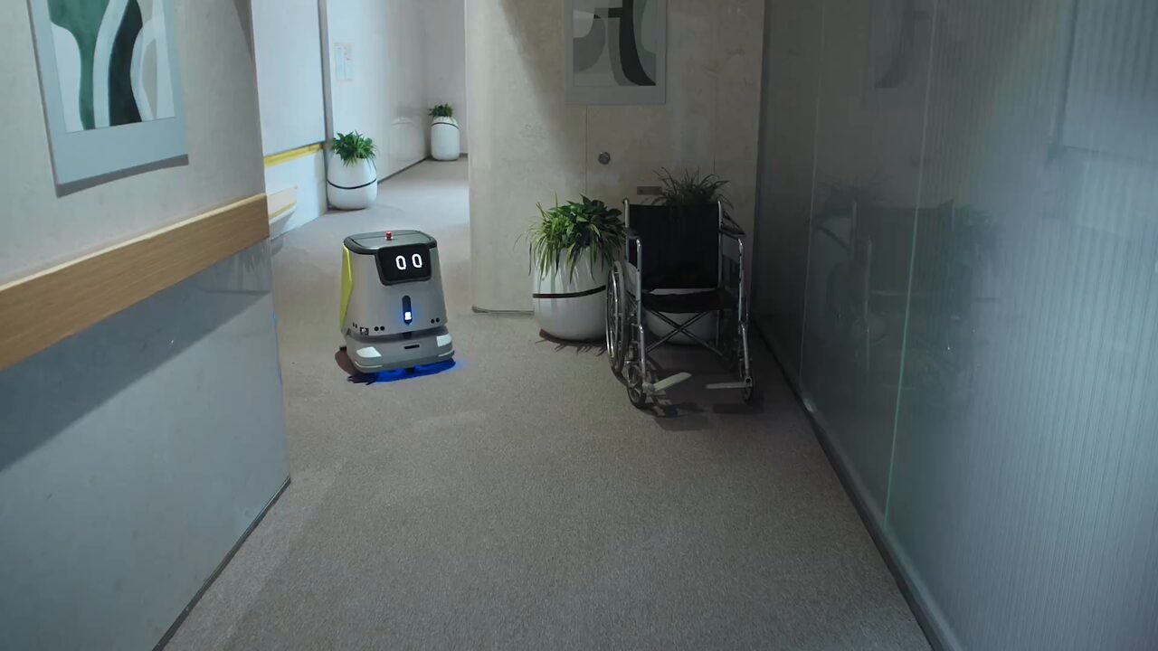 Autolaveuse autonome de la série PUDU CC1 dans la circulation d’un établissement de soins, le long d’une main courante murale.