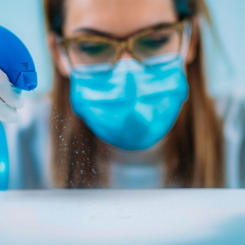 Agent d'entretien équipé d'un masque vaporisant un produit désinfectant pour le bionettoyage d'un cabinet médical à Annecy.